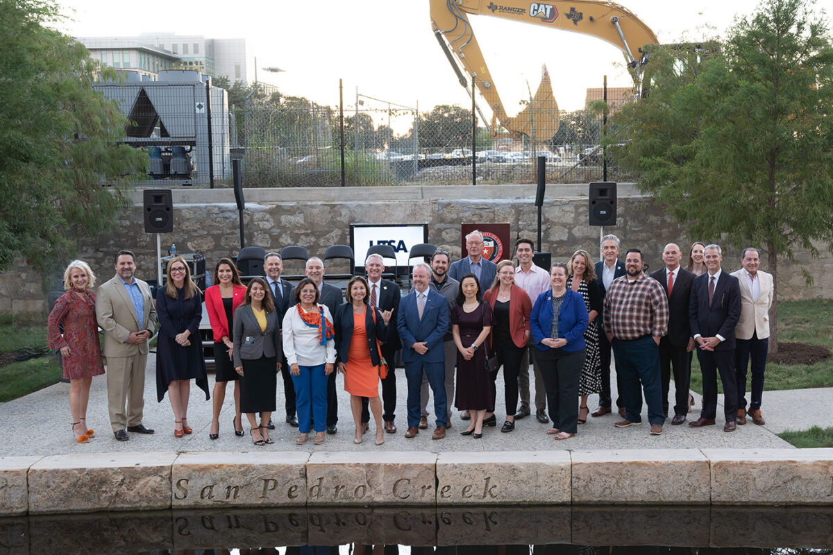 A group more than 10 people stand alongside a creek in front of a construction site.