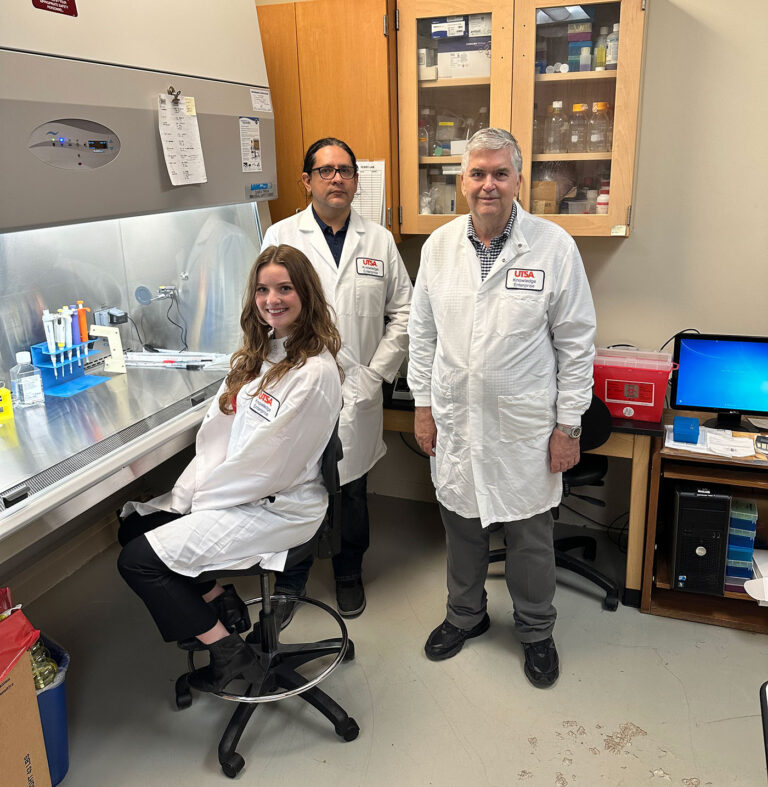 Three individuals in white lab coats stand together for a photo inside a research lab.