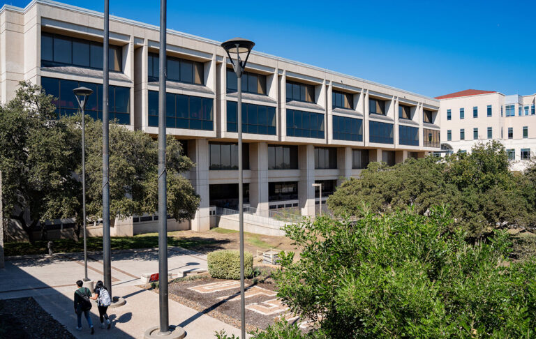 A concrete building with windows running across the side of it for three stories.