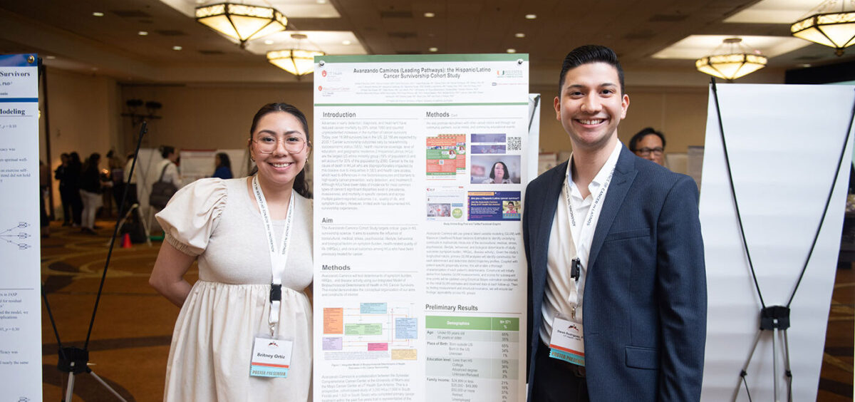 A woman and man stand side by side a large poster of text.