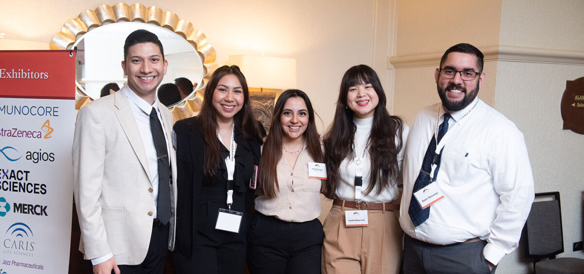 Five individuals dressed in business attire huddle together for a group photo.