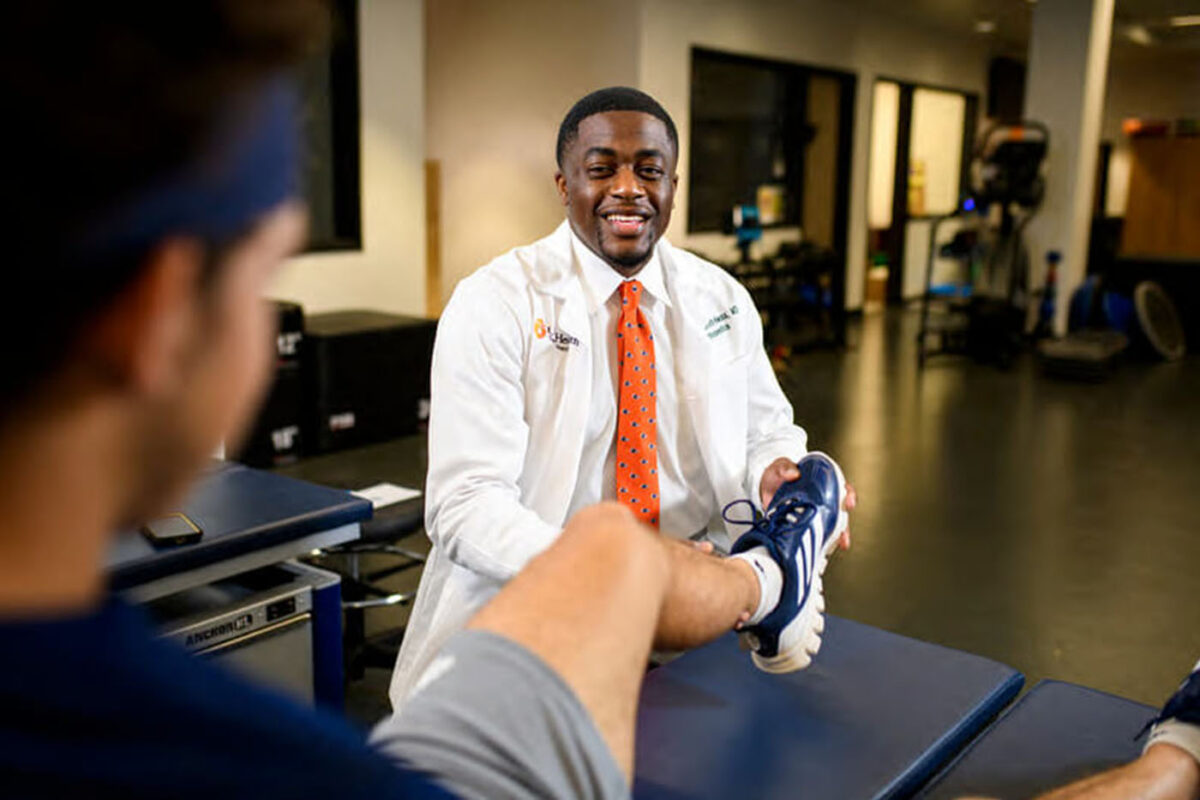 Dr. Ken Kenneth-Nwosa examines a student-athlete's left leg on a training table.