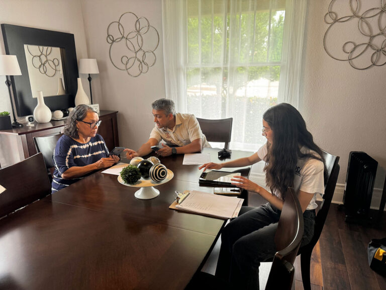Three individuals sit at a table writing and reading,