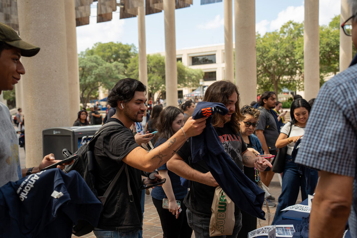 A man in a black shirt holds up a blue t-shirt he was just given.