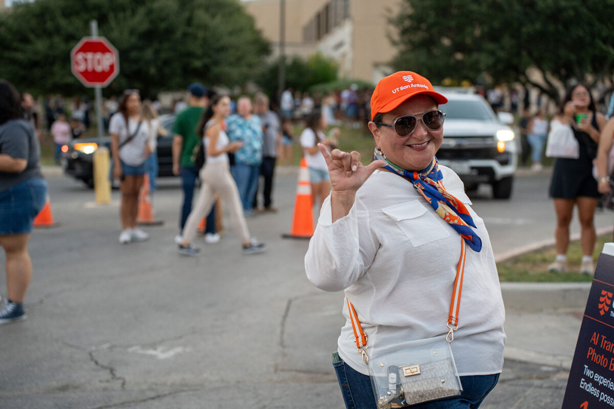A woman in an orange hat has her hand up as she sticks out her pinky, thumb and folds her index, pointer and middle finger. This gesture symbolizes a roadrunner.