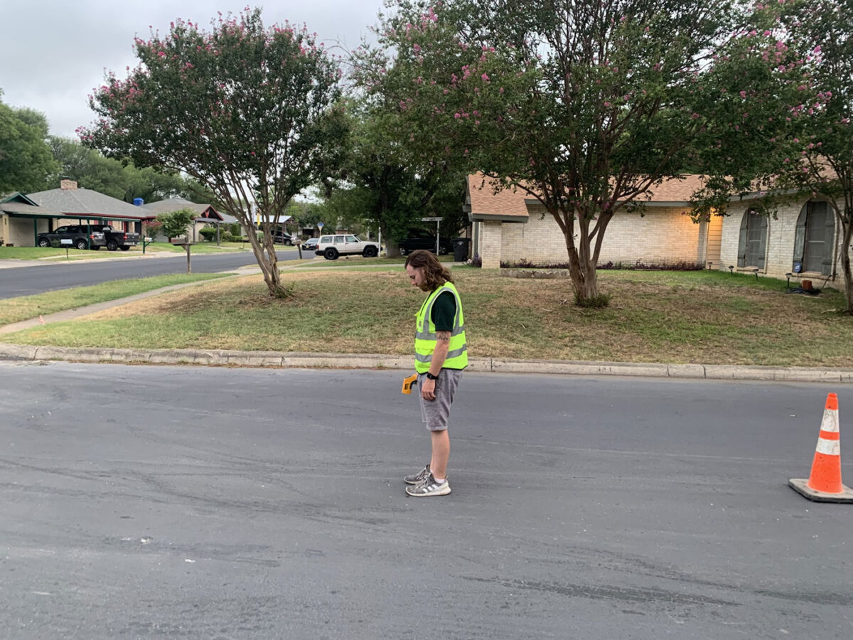 A man stands in the street with a device to record the temperature of the roadway.