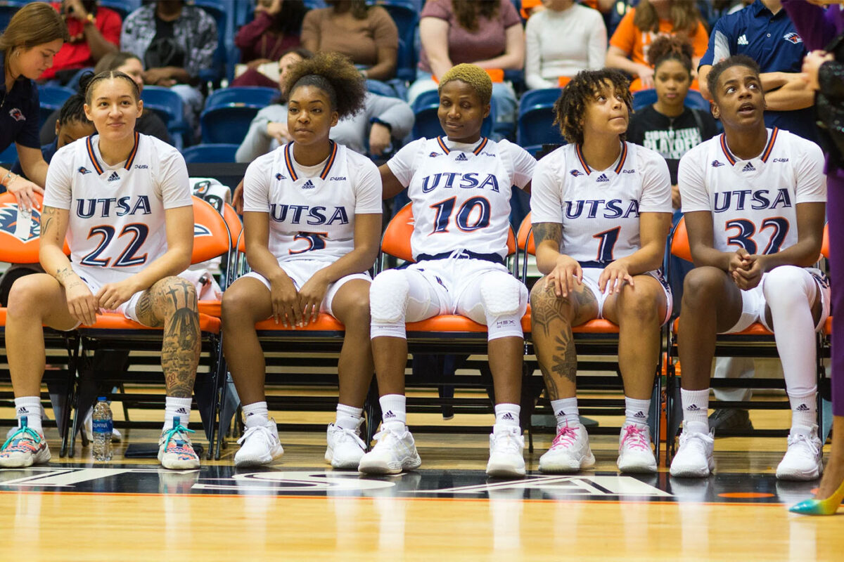 Five UTSA women's basketball players sitting in chairs on the sideline