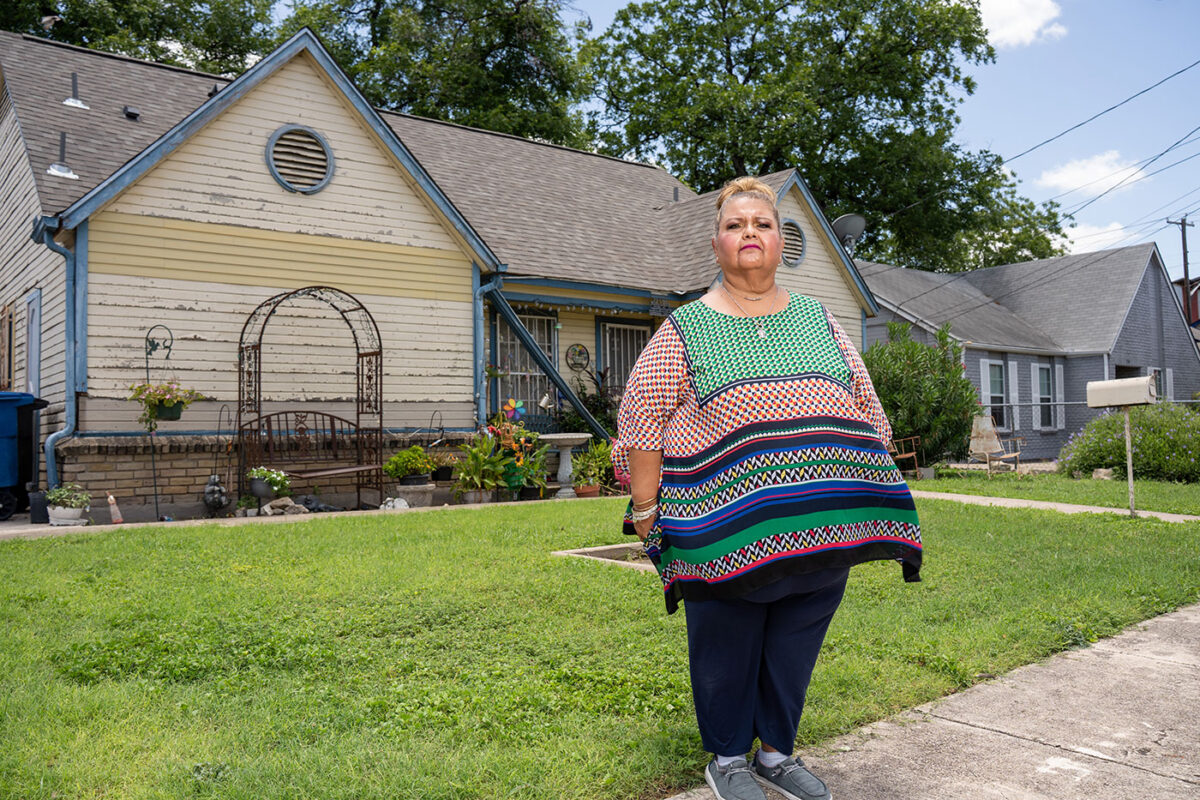 A lady stands on her front lawn and looks off to the side.