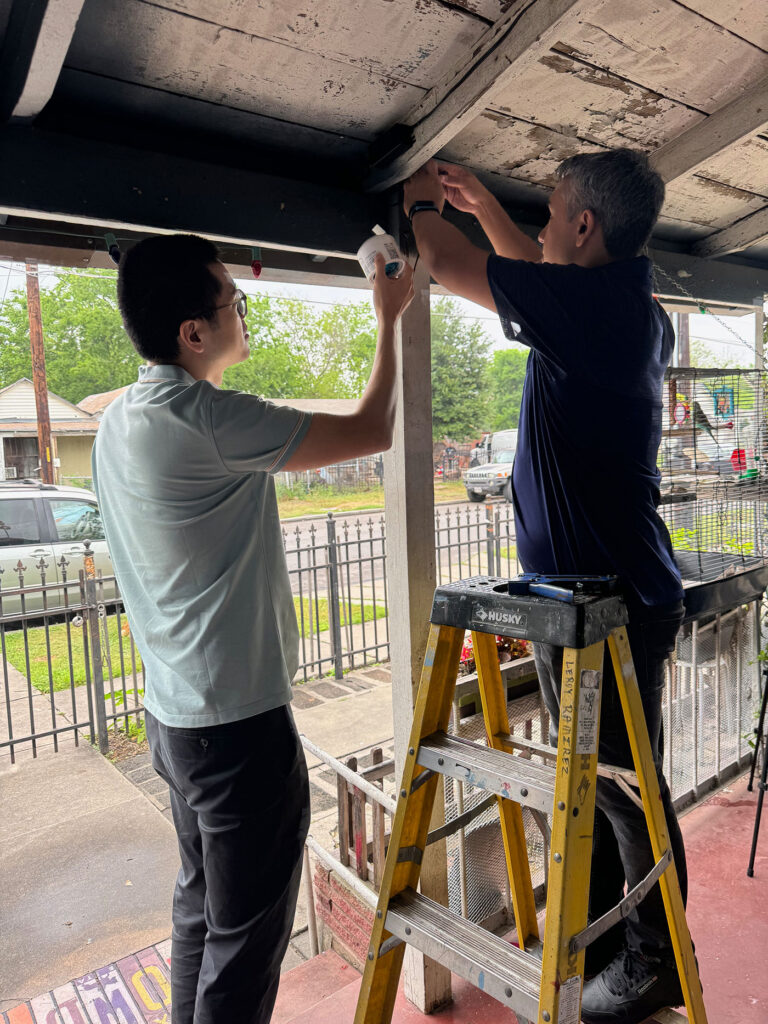 Two men install something to a pillar outside of a home.