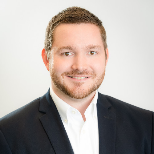 Man in a black suit with a white dress shirt smiling at the camera.