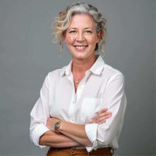 A woman in a white shirt crosses her arms and smiles.