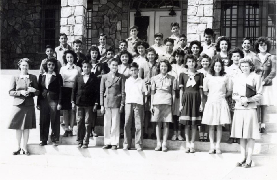 Black and white photo of young individuals standing on the steps of a building.