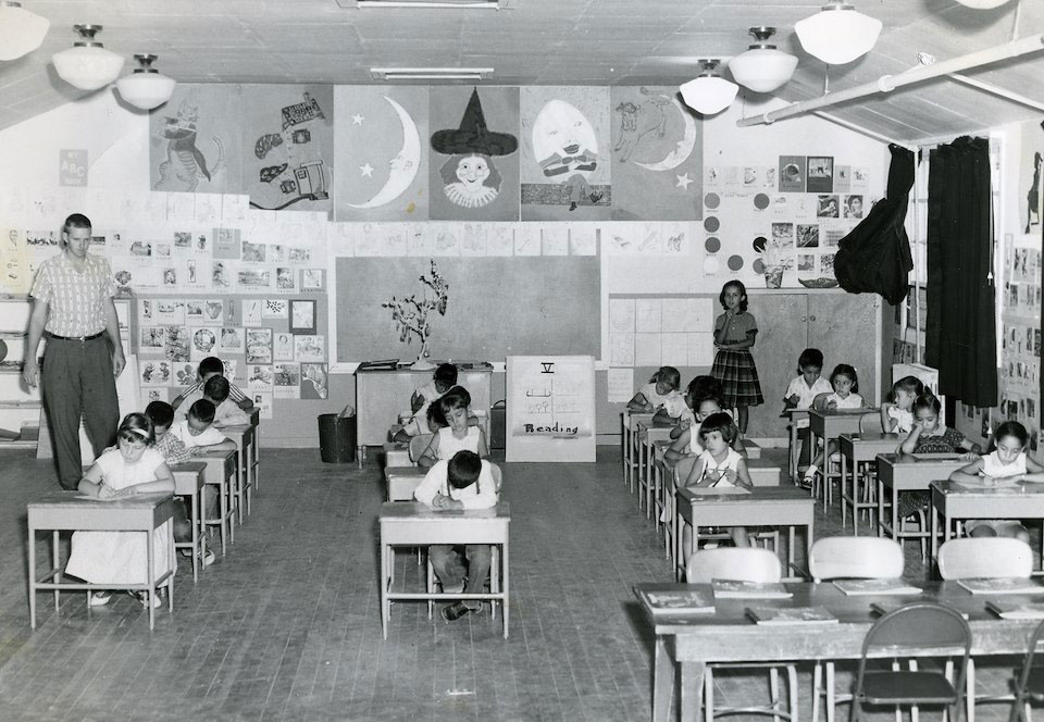 Black and white photo of elementary students sitting in a classroom at their individual desks.