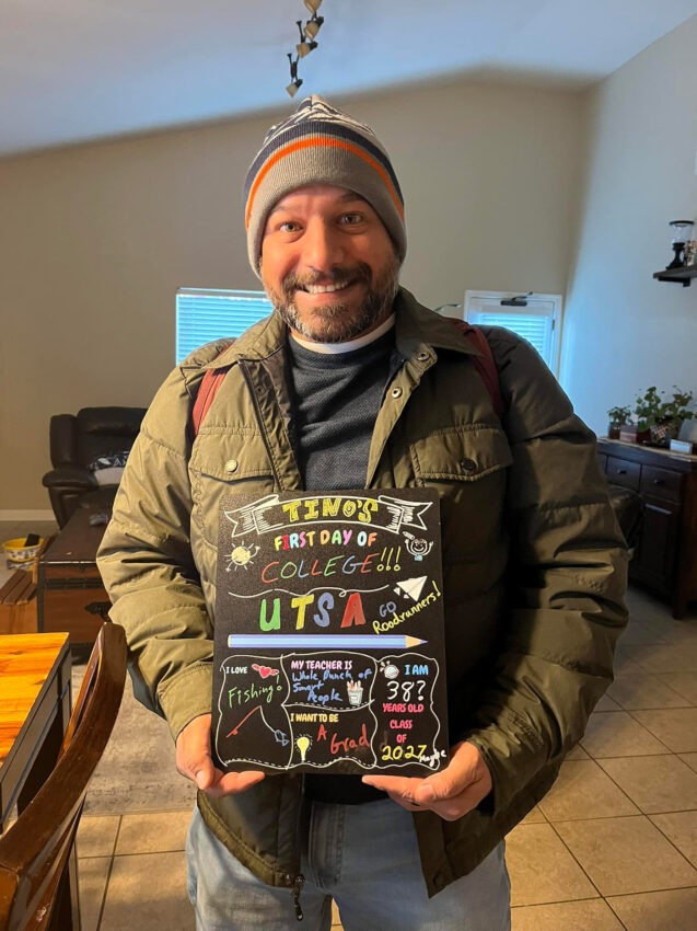 A man in a beanie and jacket holds up a sign that say, "First Day of College."