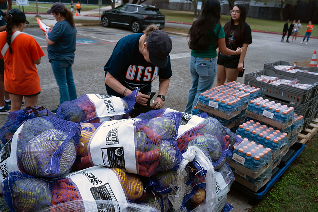 A person in a baseball cap leans over a stack of bagged veggies.