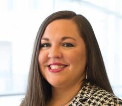 A headshot of a woman in a tweed blazer.