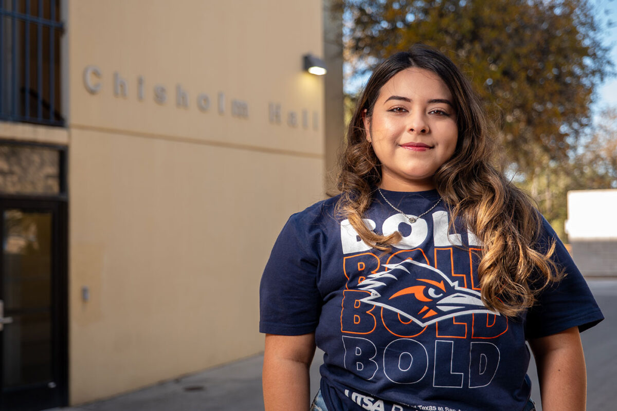 A woman wearing a blue shirt with the words, "Bold" smiles.