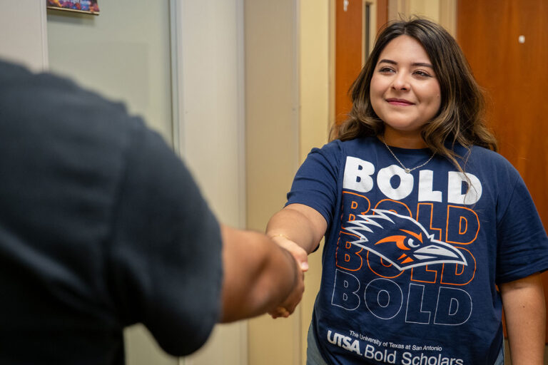 A woman holds her hand out as she shakes someone else's hand in the foreground.