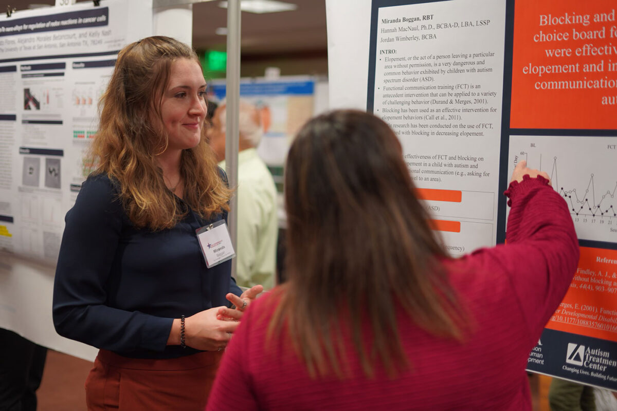 A woman with blonde hair stands beside a large poster board beside another woman.