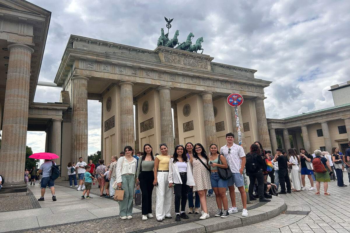 A group of young twenty something year olds stand in front of an European structure.