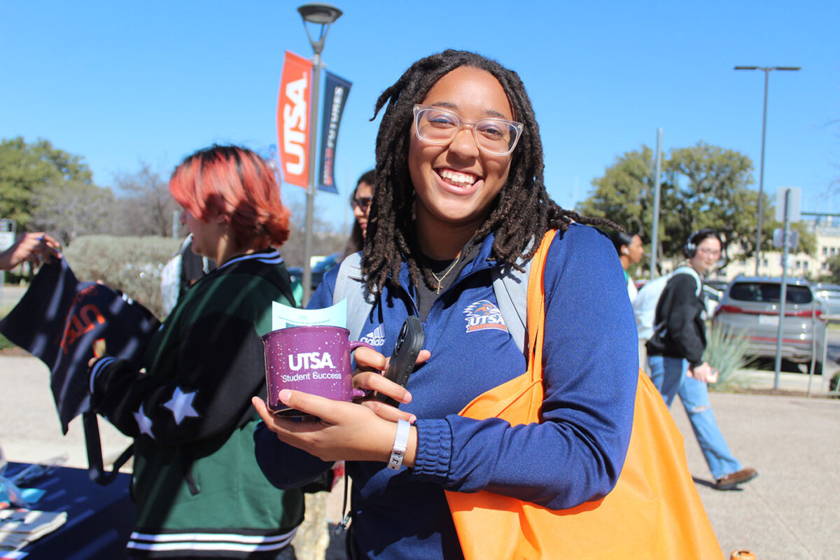 A woman with a yellow bag on her shoulder holds up a purple mug for a photo.