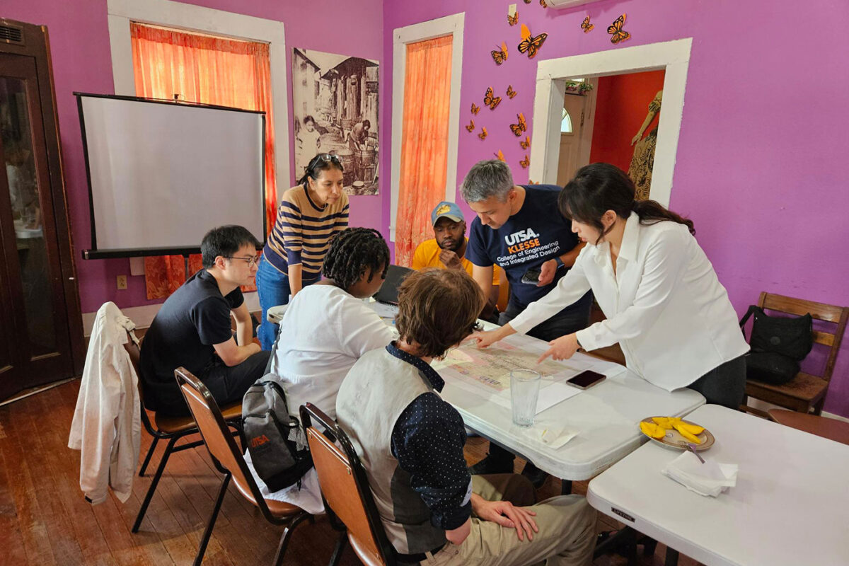 A group of people look at maps and papers on a table.