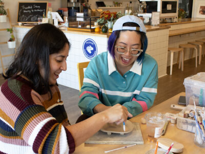Yuli Chang laughs with a young woman as they work together to sculpt a ceramic dish.