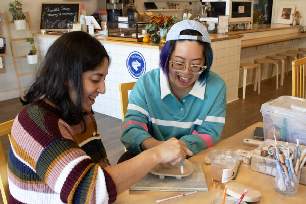 Yuli Chang laughs with a young woman as they work together to sculpt a ceramic dish.