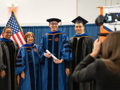 A group of four in graduation attire pose for a photographer