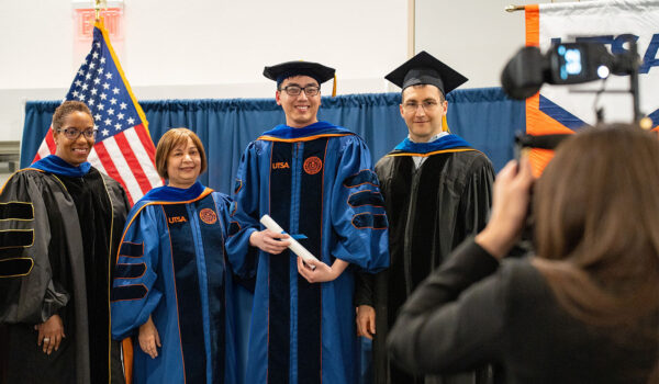 A group of four in graduation attire pose for a photographer