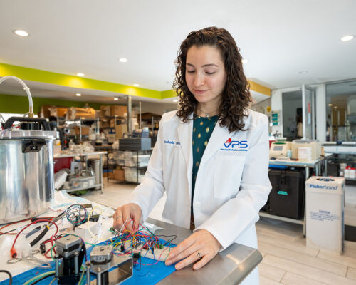 Isabella Cano adjusts electrical wires hooked to a device in a laboratory