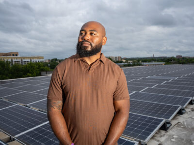 Jamal Hasty stands in front of solar panels on a rooftop at the Pearl