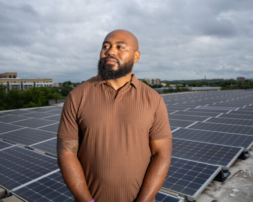 Jamal Hasty stands in front of solar panels on a rooftop at the Pearl