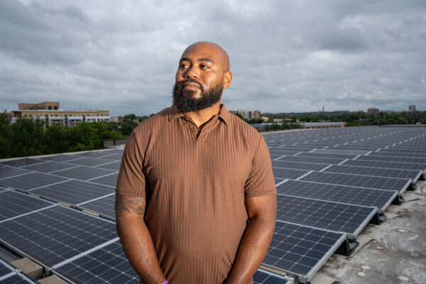 Jamal Hasty stands in front of solar panels on a rooftop at the Pearl