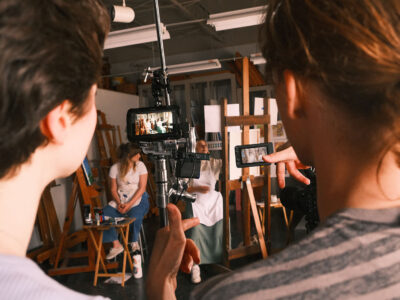 Two students look a camera monitor as two other students take their marks in a scene