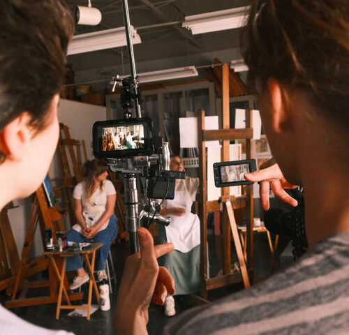 Two students look a camera monitor as two other students take their marks in a scene