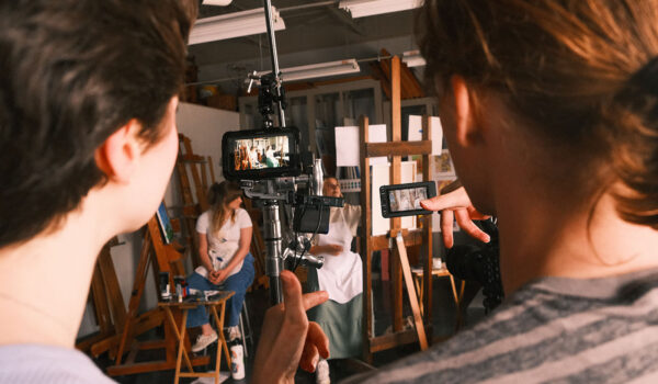 Two students look a camera monitor as two other students take their marks in a scene