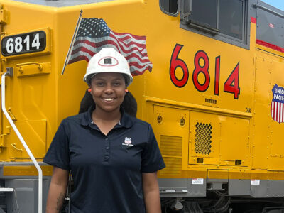 Taylor Richard poses in front of a large yellow locomotive