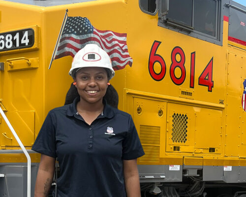 Taylor Richard poses in front of a large yellow locomotive