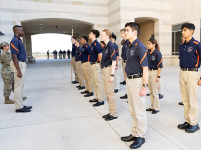 Cadets in blue polos stand at attention in the north breezeway of the Recreation Wellness Center.