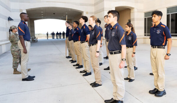 Cadets in blue polos stand at attention in the north breezeway of the Recreation Wellness Center.