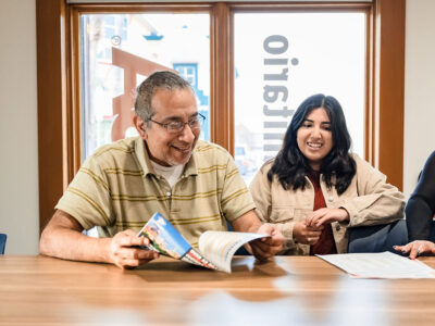 An elderly man sits at a table with a paper in his hand as an ambassador from the UT San Antonio Westside Community Center.