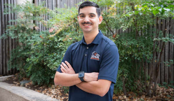 A man in a blue polo folds his arms and smiles.