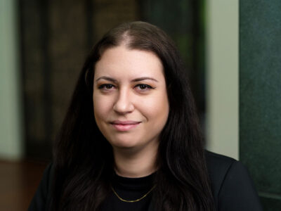 A woman with long black hair in a black shirt and blazer smiles at the camera.