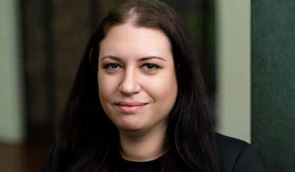 A woman with long black hair in a black shirt and blazer smiles at the camera.