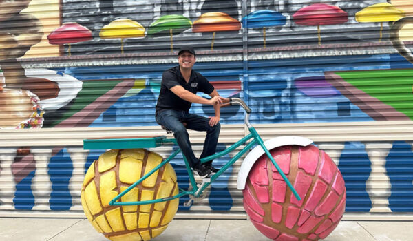 A man sits on top of a bike, which has wheels that resemble conchas, a mexican pastry,