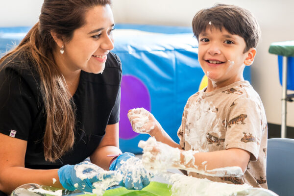 A little boy smiles at the camera beside a woman.
