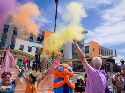 Colored smoke goes off as people cheer and clap in front of the MAC building.