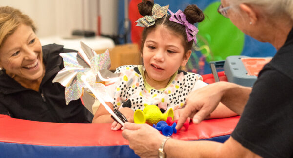 A child sits in a foam activity pool with two medical physicians.