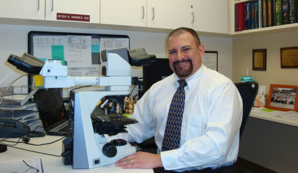 A man in an office setting in front of a microscope.